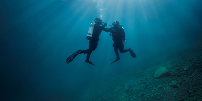 Escena bajo el agua: un buceador ayuda a otro que tiene problemas con el suministro de aire.